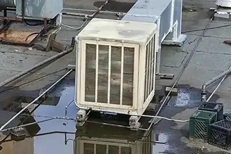 Swamp cooler on a flat roof with water pooled around its base